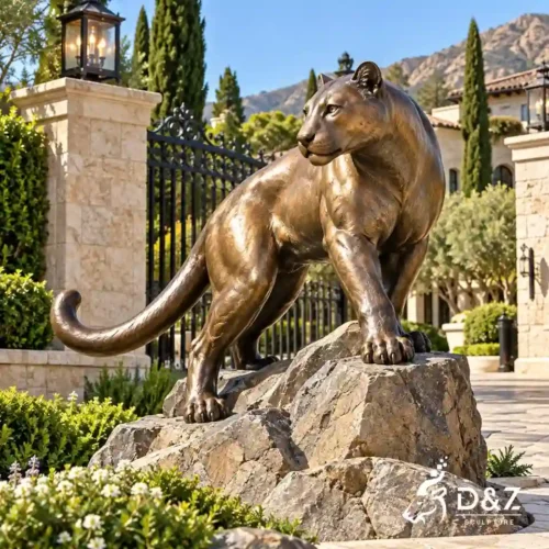 Bronze cougar sculpture standing on a rock formation and looking back beside a wrought iron estate gate.
