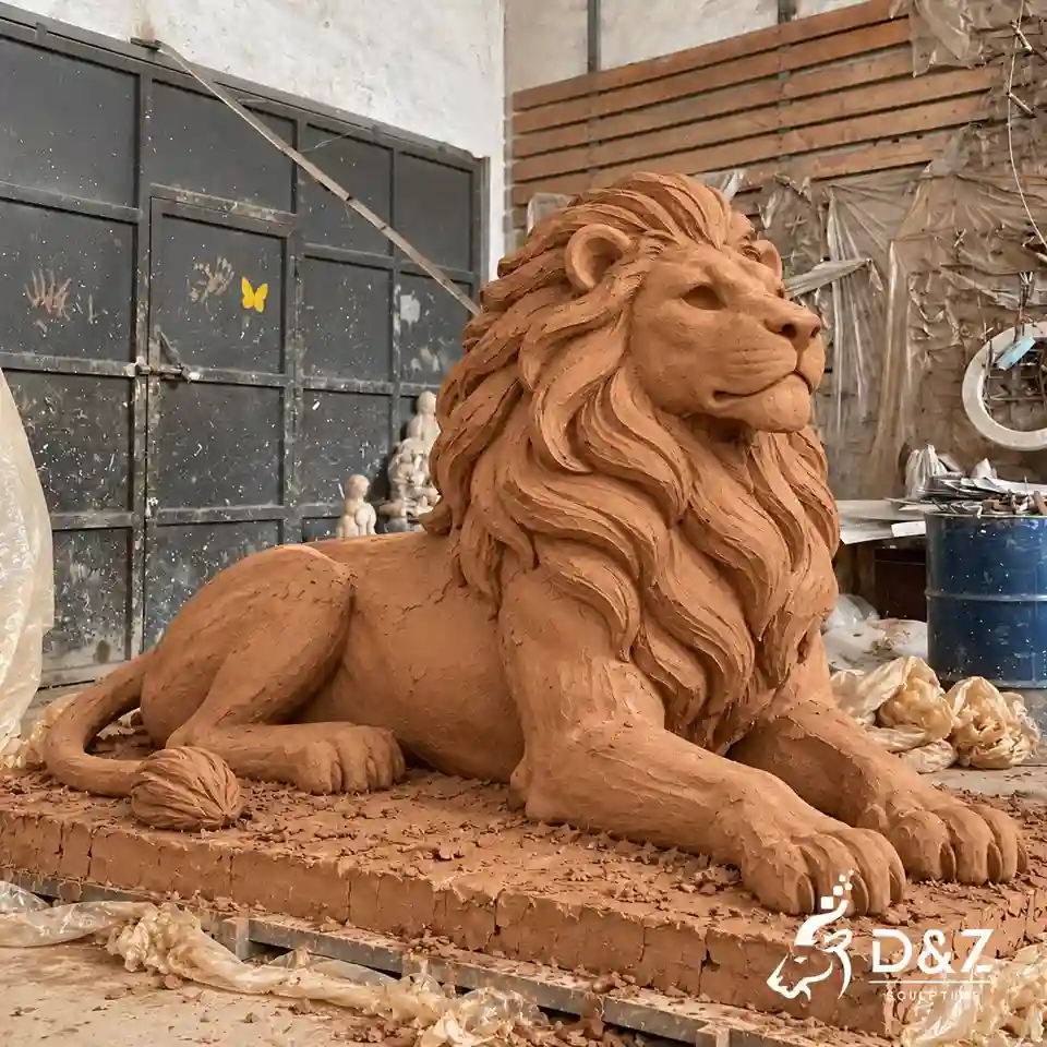 Unpainted reclining lion clay model with simplified sculpted mane and hollow eye details in a sculpture workshop Unpainted reclining lion clay model with simplified sculpted mane and hollow eye details in a sculpture workshop